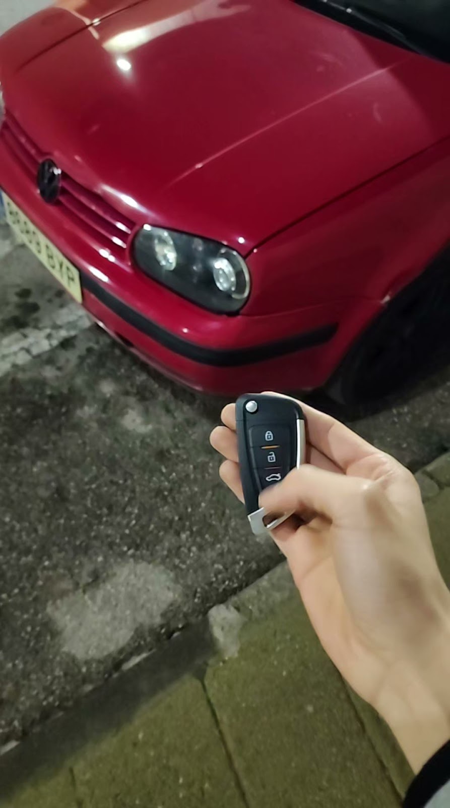 Mando de coche entregado de noche frente a un Volkswagen rojo